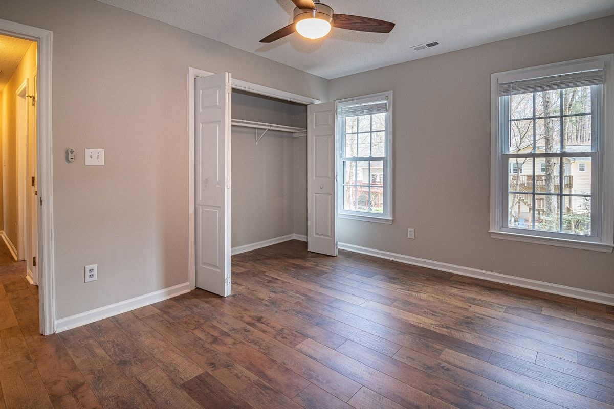 Empty bedroom with wood-look floors, open closet, and a ceiling fan light on